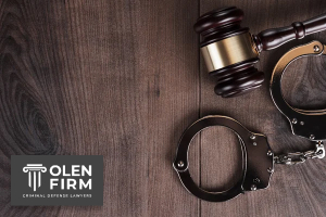 Gavel and handcuffs on a wooden table with Olen Firm logo.