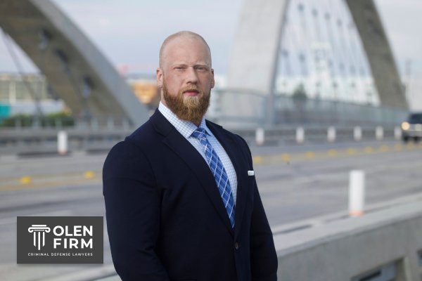 Jared Olen is in a suit, standing outside, wearing a blue tie. The logo in the corner reads "Olen Firm."
