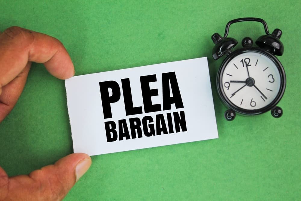 An alarm clock next to a hand holding a white paper with the words "Plea Bargain," symbolizing the concept of a court appeal.