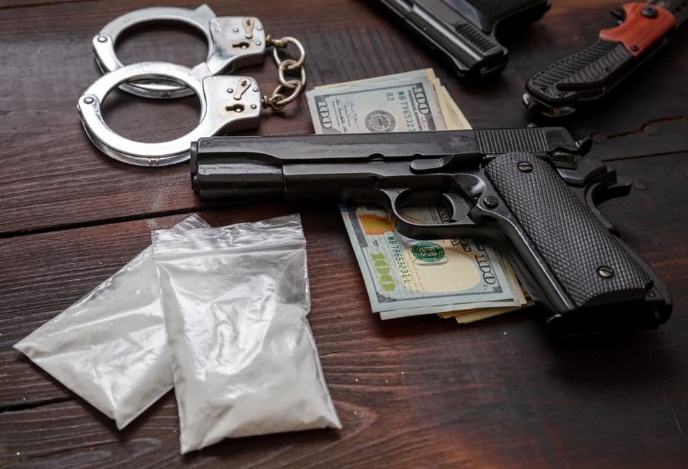 Plastic packets of cocaine, a pistol, U.S. dollars in banknotes, and handcuffs. Concept of drug possession, use, arrest, and penalties for illegal narcotics trade.