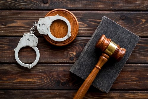 Judge’s gavel, handcuffs, and a legal book on a wooden table, symbolizing criminal justice and law enforcement.