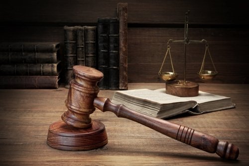 Wooden gavel, open law book, and justice scales on a wooden desk, representing court and legal judgment.